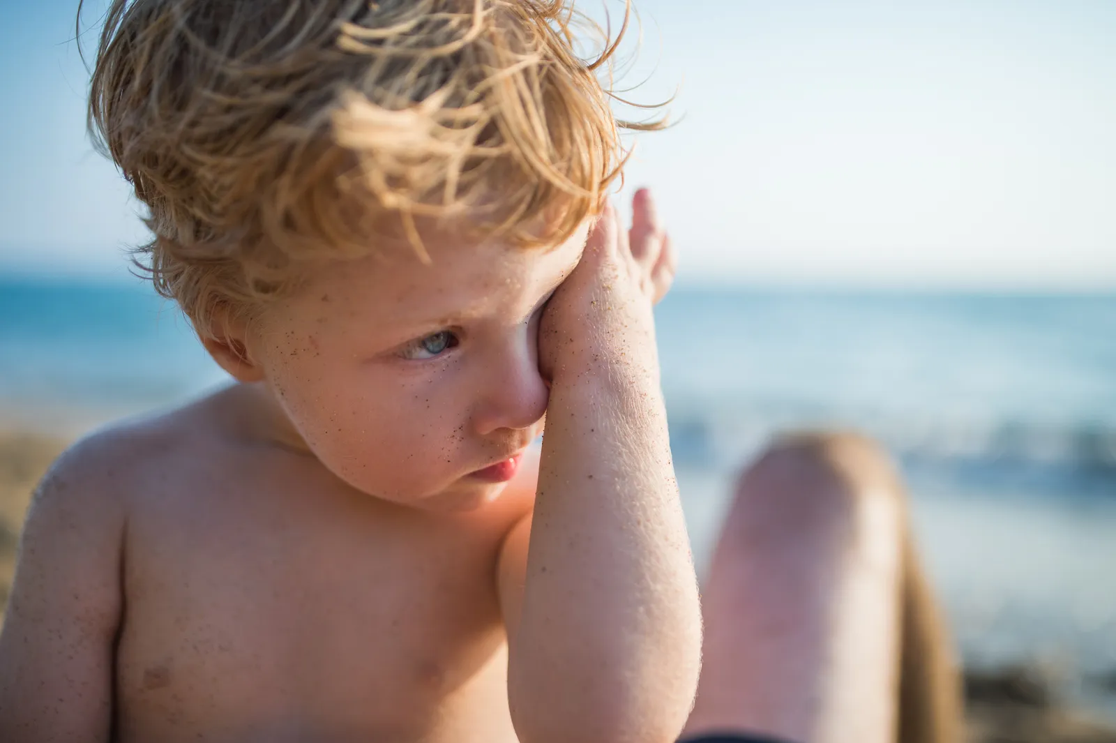 Nahaufnahme, kleiner blonder Junge am Strand reibt sich am Auge.