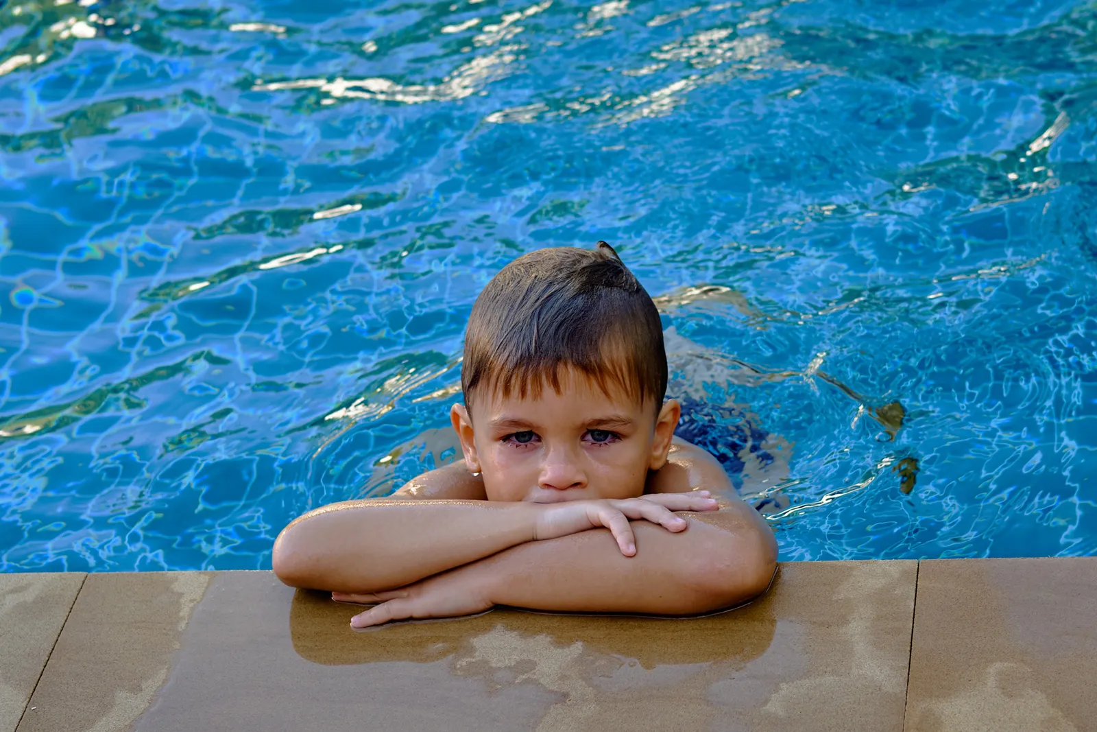 Kleiner Junge mit roten Augen am Schwimmbeckenrand