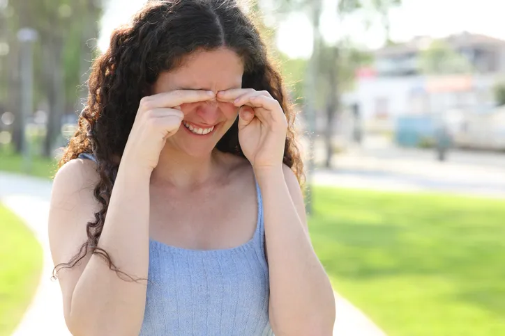Frau in einem Park reibt sich die Augen. Es ist Sommer.