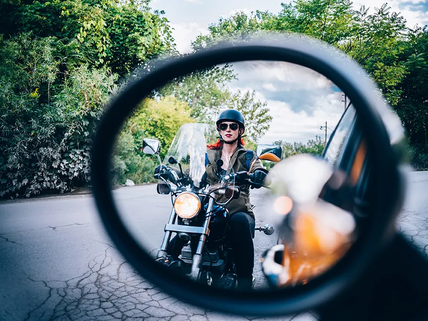 Frau auf Motorrad im Rückspiegel eines Autos