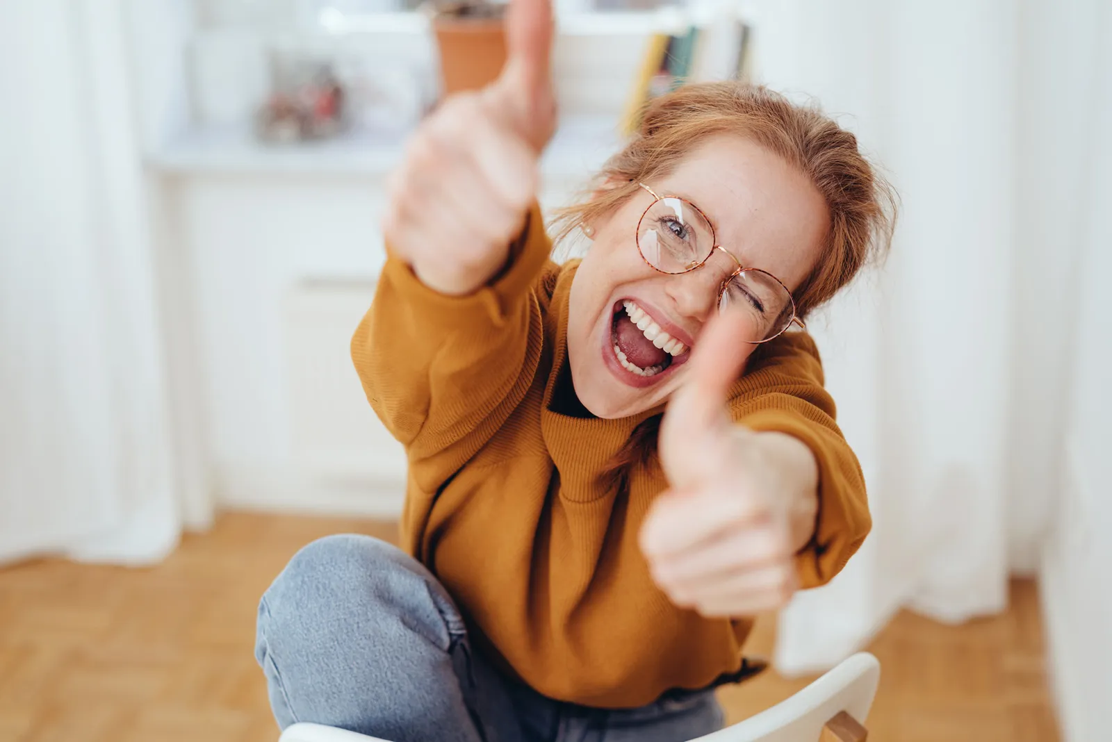 Junge Frau mit Brille zeigt Daumen hoch und lacht