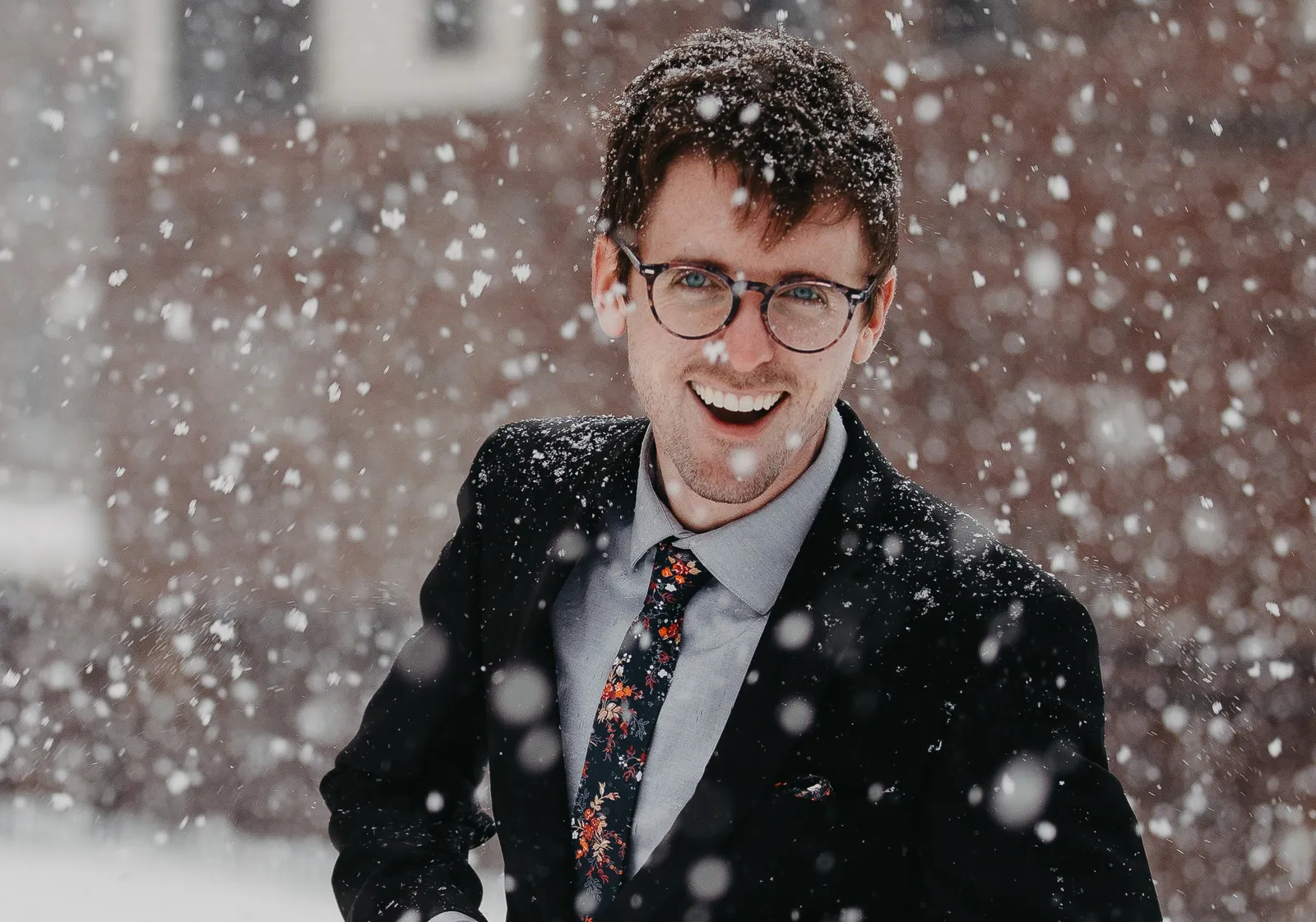 Junger Mann im Anzug mit Brille bei Schneefall