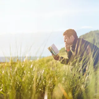 Mann sitzt am See und liest in einem Buch