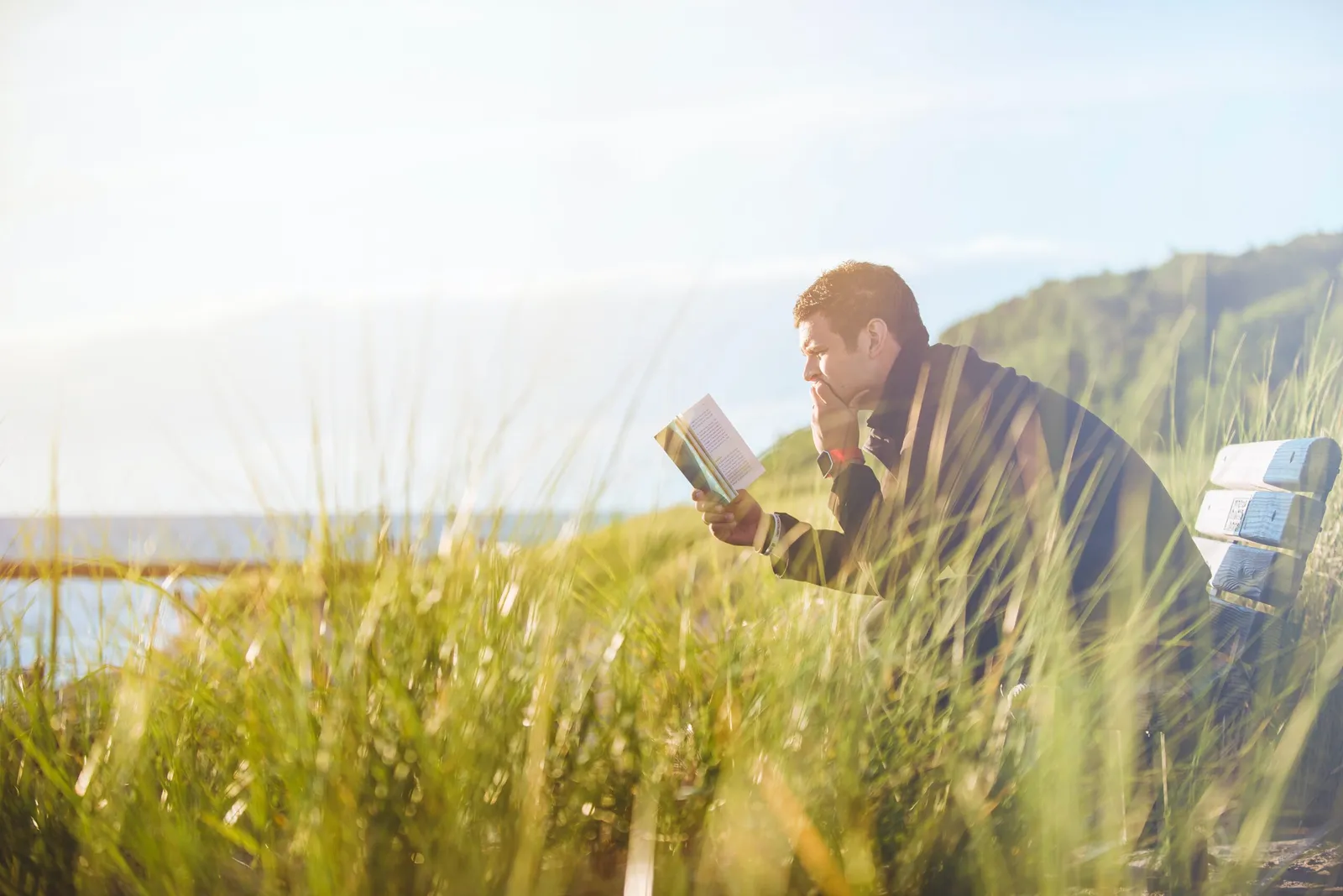 Mann sitzt am See und liest in einem Buch