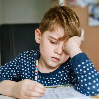 Schuljunge sitzt motivationslos über Schulheft